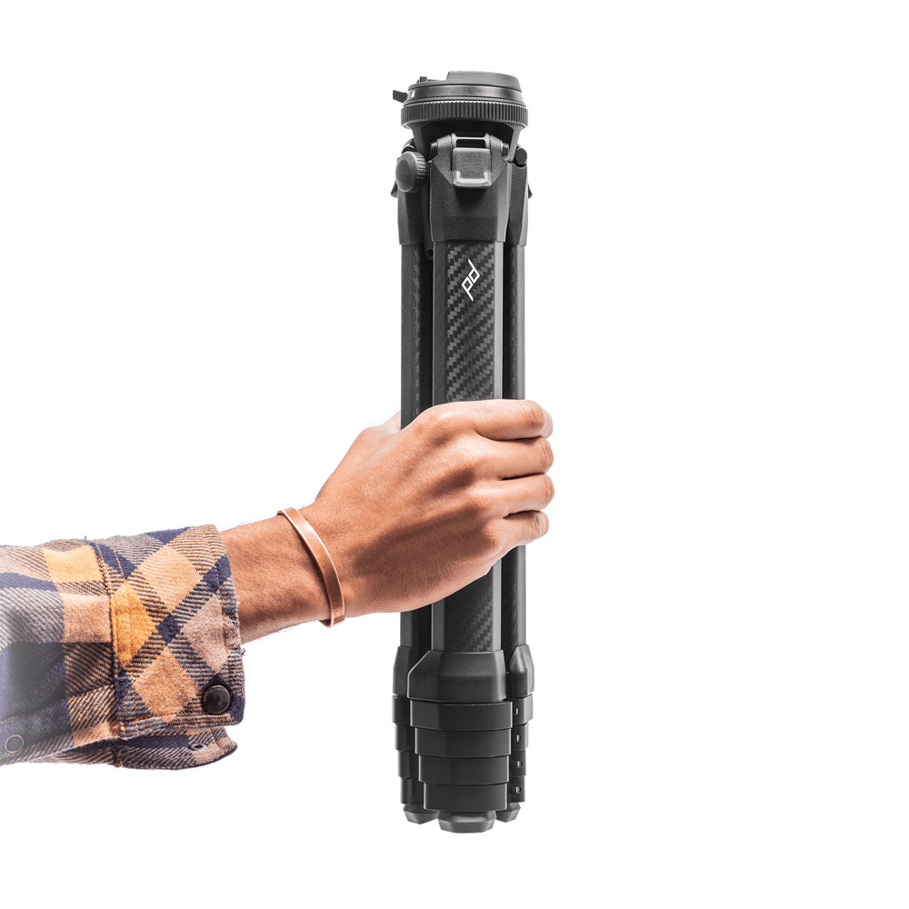 Peak Design Travel Tripod being held by a woman's hand against a white background. 
