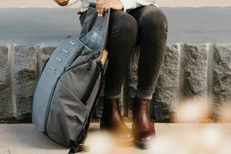 The Peak Design Everyday Backpack being opened while on the ground next to a woman. 